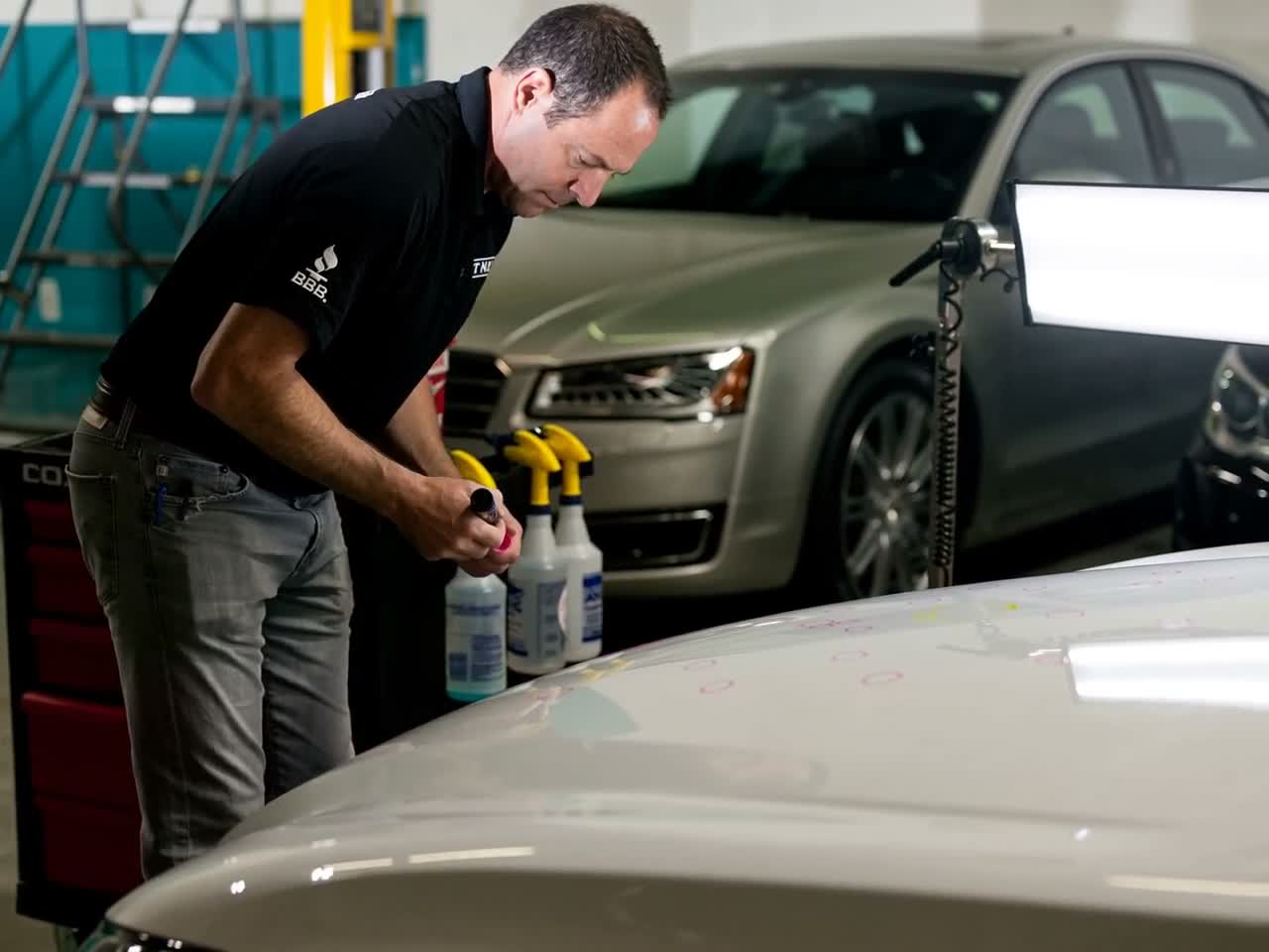 Technician inspecting and marking a vehicle hood under a repair light
